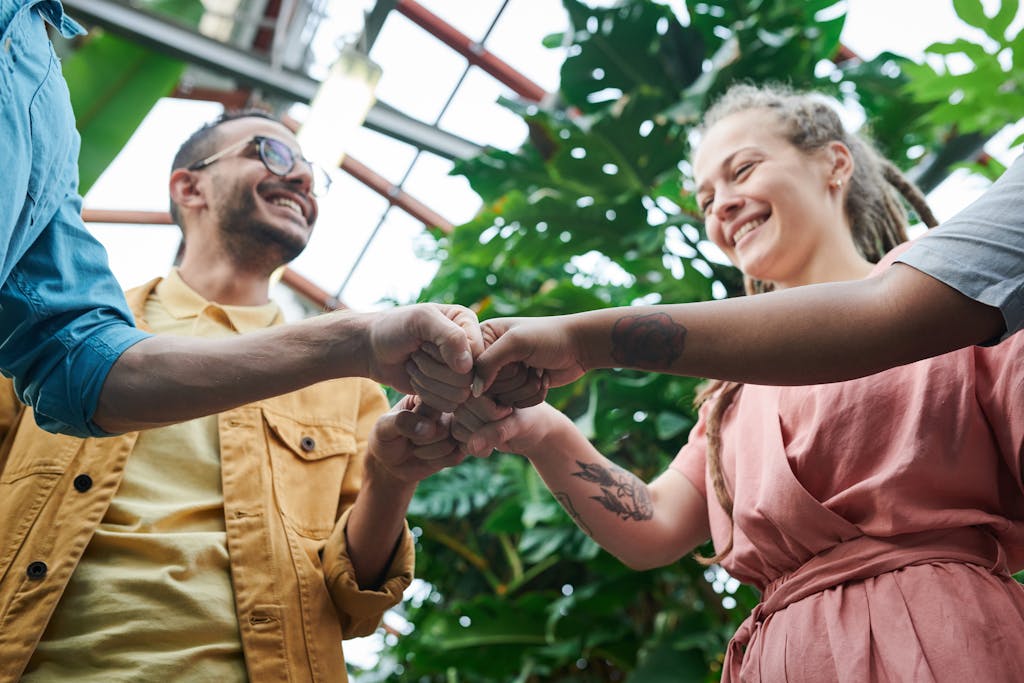 A group of young adults celebrating teamwork with a fist bump in a lush outdoor setting.